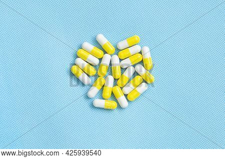 Yellow-white Pills On Blue Background. Top View Of Vitamin Supplements. Medical Concept.