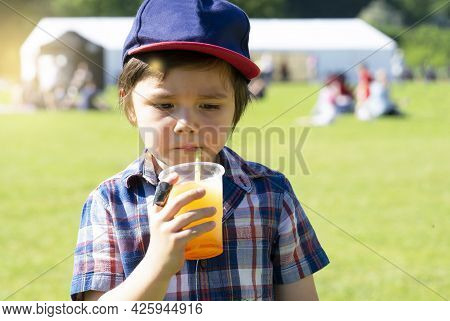 High Key Portrait Of Kid Boy Drinking Orange Slush From Plastic Glass In Hot Sunny Day,thirsty Child