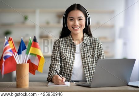 Smiling Asian Lady Using Laptop And Headset, Learning Foreign Language