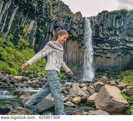 Iceland. Hiker enjoying majestic Svartifoss waterfall. Female is visiting famous tourist attraction of Iceland. Spectacular natural landmark on vacation in Skaftafell. Icelandic nature landscape.