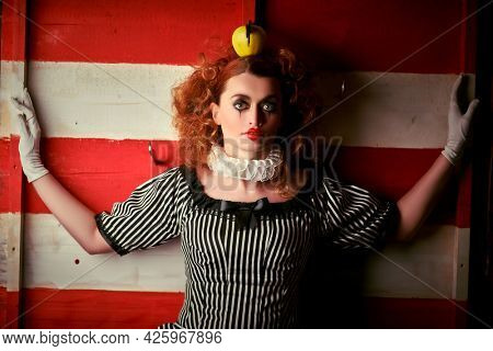 Circus performer girl in a clown costume performs a knife throwing trick. The dark circus concept. Retro style.