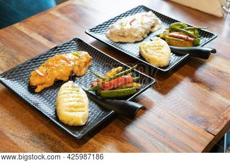 Side Shot Showing Two Asthetic Black Square Plate With Handle Placed On Wooden Table Filled With Whi