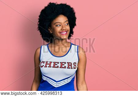 Young african american woman wearing cheerleader uniform looking away to side with smile on face, natural expression. laughing confident. 