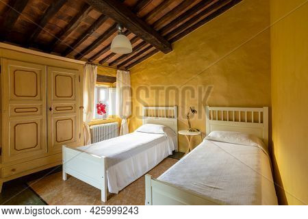 Interior of a bedroom with two single beds. Spartan ambiance and nothing luxurious. The walls are yellow and it is an old Italian house from Tuscany