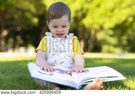 Little Girl, Child Is Studying A Book. Early Toddler Development, Delight Baby Outdoors In The Park.