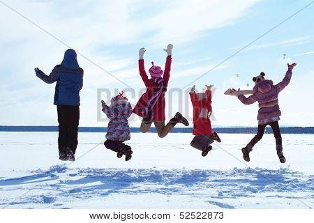 Group of cheerful children jumping in the snow in winter