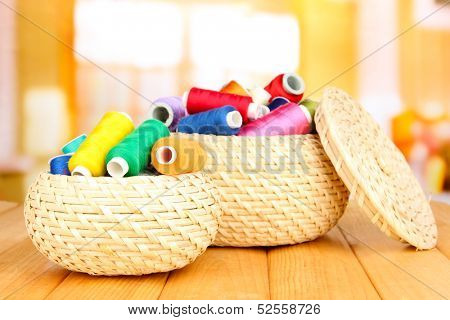 Wicker baskets with accessories for needlework on wooden table, on bright background