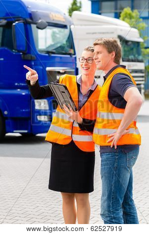 Logistics - proud driver or forwarder and female coworker with tablet computer, in front of trucks and trailers, on a transshipment point, its a good and successful team