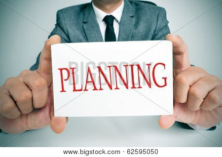 businessman sitting in a desk showing a signboard with the text planning written in it