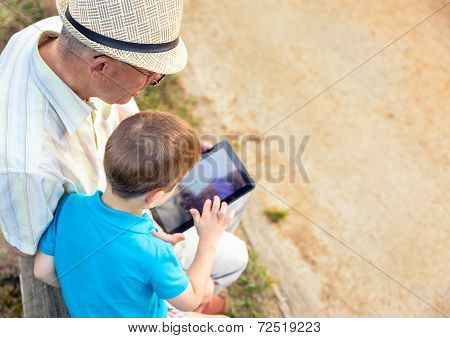 Grandchild And Grandfather Using A Tablet Outdoors