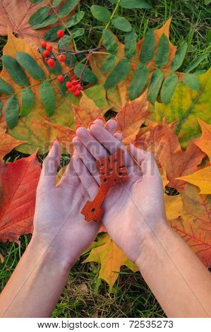The antique wooden Ethiopian Orthodox traditional cross in the woman's palms. Autumn leaves on backg