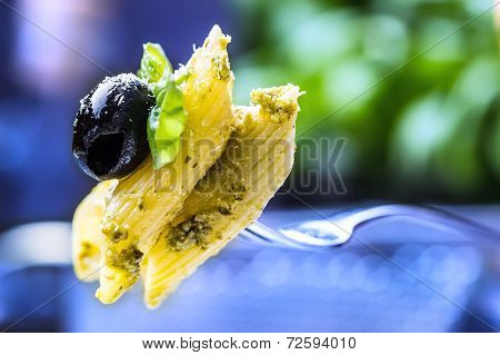 Serving of penne pasta on a fork with basil leaves and black olive.