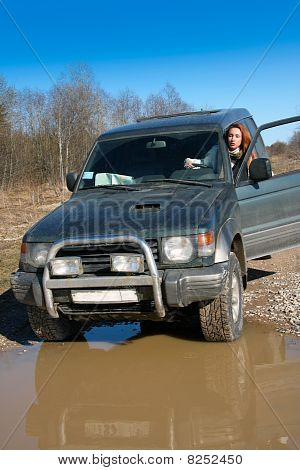 Unga kvinnan bakom rodret av offroad bil på grusväg innan vatten hinder