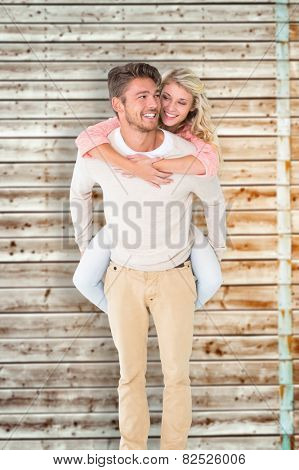 Handsome man giving piggy back to his girlfriend against faded pine wooden planks