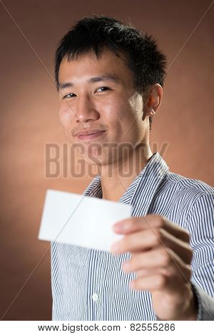 Young Chinese frank businessman holding blank white business card, closeup portrait in studio.