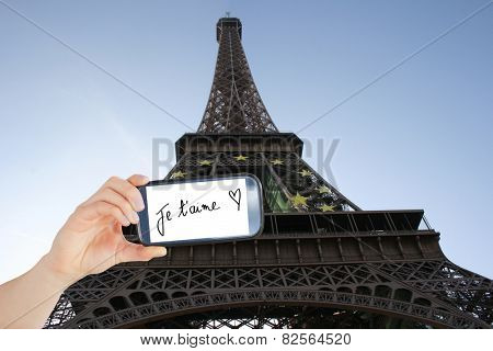 Composite image of hand holding smartphone showing je taime against eifell tower
