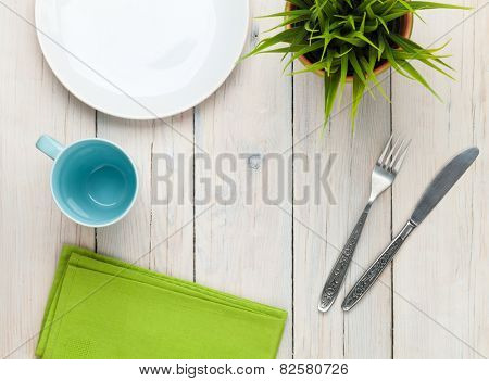 Empty plate, cup and silverware over white wooden table background. View from above with copy space