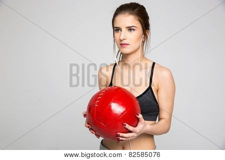Beautiful sports woman holding medicine ball over gray background