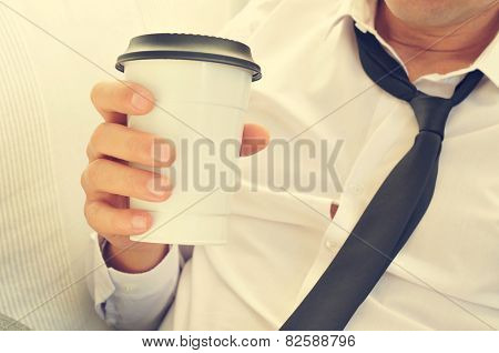 a young man with his necktie loosened drinking coffee in a paper cup