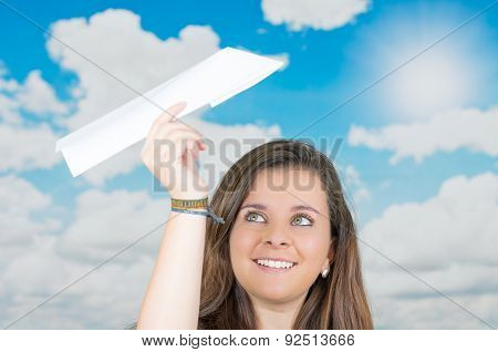 brunette holding a paperplane in front of cloud themed background