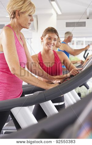 Woman On Running Machine In Gym Encouraged By Personal Trainer