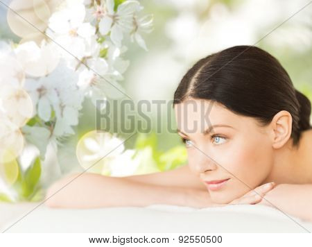 people, beauty, spa and body care concept - happy beautiful woman lying on massage desk over green natural cherry blossom background