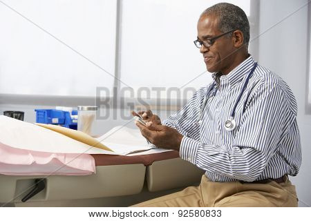 Male Doctor In Surgery Using Mobile Phone