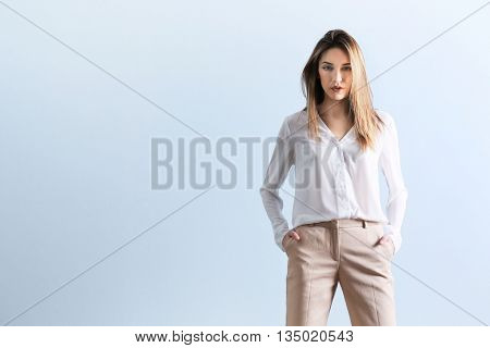 Beautiful young woman in a white shirt and beige pants on blue wall background