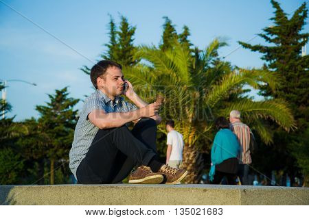 Young man at promenade eating an ice-cream and using his phone, maybe he is single or waiting for someone.