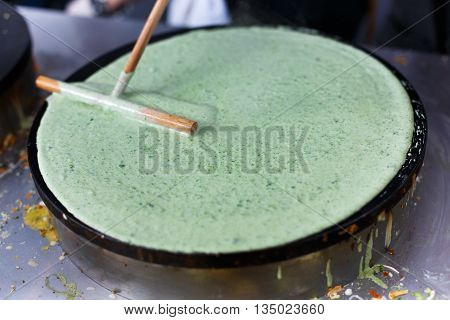 Making spinach crepe. Vegetable green crepe or pancake made by street vendor at outdoors creperie. French cuisine, cooking, commercial kitchen.