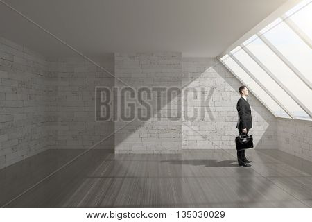 Businessman holding briefcase in empty loft interior with brick wall cocrete ceiling dark wooden floor and window. 3D Rendering