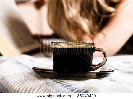 beautiful woman reading a thick book lying on the bed, close-up coffee cup.