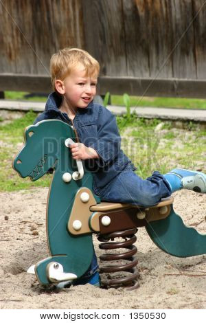 Niño escalada en dinosaurio de juguete en un patio de recreo