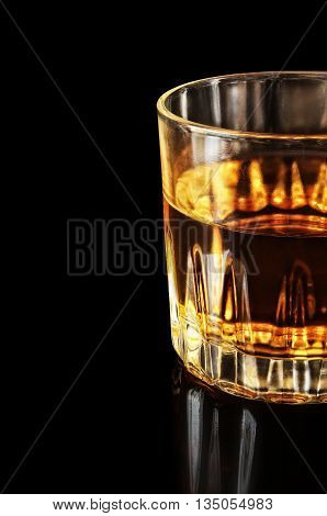 Part of a glass with alcohol on a black background. The object is located a shot on the right. Part of object. Reflection from a surface. Indoors. Vertical format. Color. Photo.