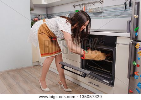 young housewife taking cupcakes from oven and smiling