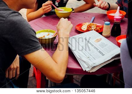 Kuala Lumpur Malaysia - March 17 2016: Group of young people having a breakfast with congee and Youtiao in Chinatown Kuala Lumpur Malaysia on March 17 2016.