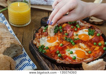 Hand of the girl dip bread into eggs a la flamenca. Spanish cuisine.