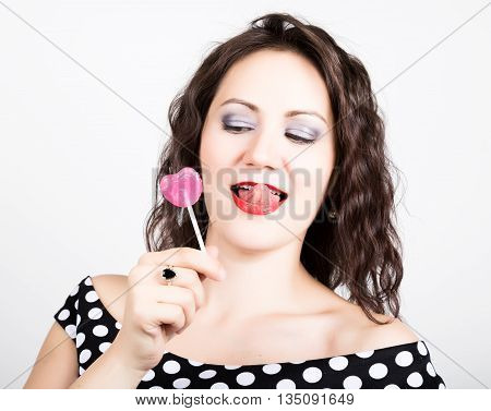 Portrait of happy beautiful young woman licking chupa chups. pretty woman with heart shaped lollipop.