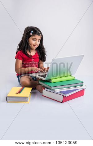 cute little indian girl studying on laptop, asian small girl studying and using laptop, innocent indian girl child and study concept with pile of books & laptop