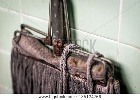 The dirty old mop with rust  on old green tile background.