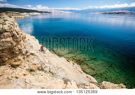 Mountain biker riding on bike in summer inspirational mountains and sea landscape view. Man cycling MTB on enduro dirt and rocky trail track. Fitness motivation beautiful inspirational view Croatia.