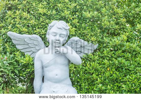 Closeup beautiful cement angle statue on blurred green plant textured background