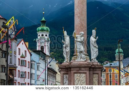 A view along Maria-Theresien-Strasse in Innsbruck during the day. The Annasaule Hospital Church and other buildings can be seen. Mountains can be seen in the distance.