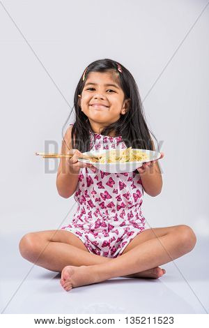 Happy Asian child eating delicious noodle, cheerful little indian girl posing with noodles in white dish isolated over white background, girl eating noodles