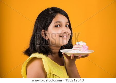 portrait of Indian kid eating cake or pastry, cute little girl eating cake, girl eating strawberry cake over yellow background
