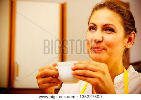 Mature Woman Drinking Cup Of Coffee In Kitchen.