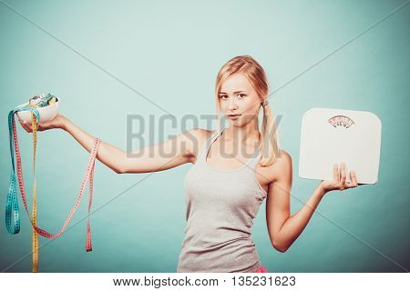 Diet healthy eating and slim body concept. Fit fitness girl holding bowl with many colorful measuring tapes as dieting symbol and weight scales studio shot on blue