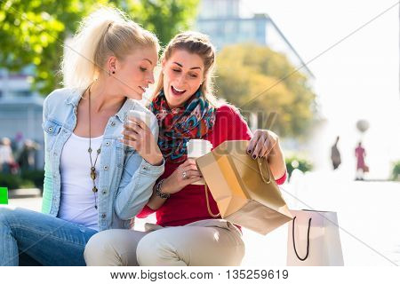 Two women friends sitting on fountain rim in city with shopping bags