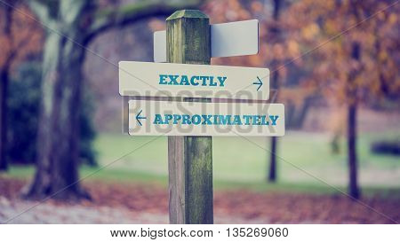 Signpost in a park or forested area with arrows pointing two opposite directions towards Exactly and Approximately.