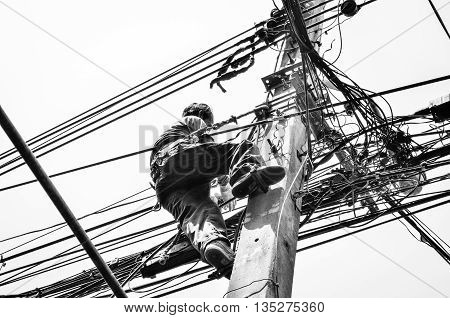 Black and White in Silhouette photo effect. Electricians repairing wire at climbing work on electric post power pole